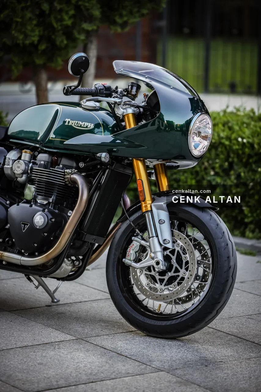 Yeşil Triumph café racer, yuvarlak far ve altın çatal, yakından
