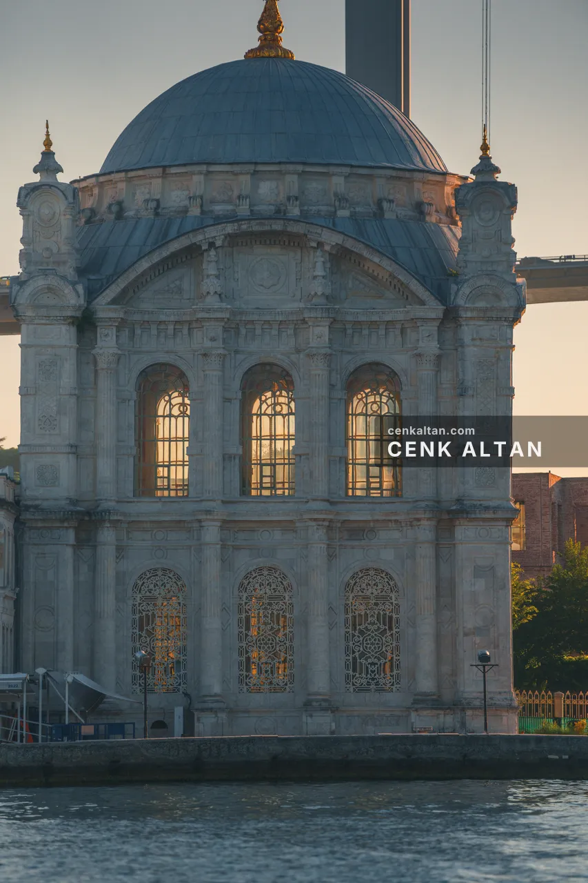 Sabah, Ortaköy Camii'nin kubbesi ve kemerli pencereleri; camlarda güneş, arkada köprü ayağı