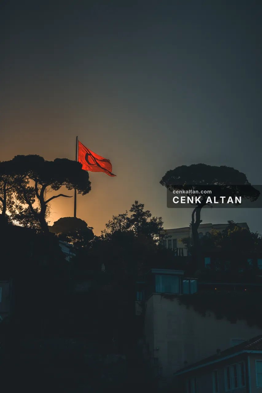 Alacakaranlıkta turuncu gökle aydınlanan Türk bayrağı, iki fıstık çamı silueti; aşağıda beyaz köşk çatısı