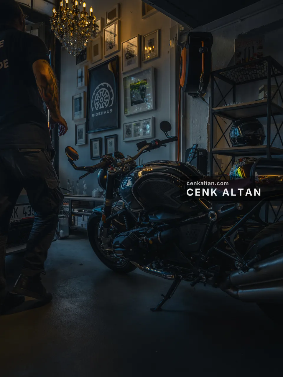 Duvarları çerçevelerle dolu bir garajda siyah motosiklet ve avize