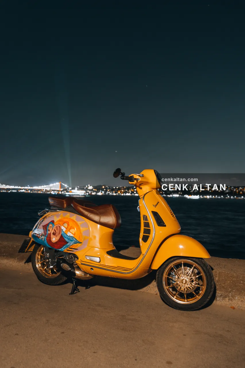 Gece rıhtımda sarı Vespa ve uzakta ışıklı kıyı