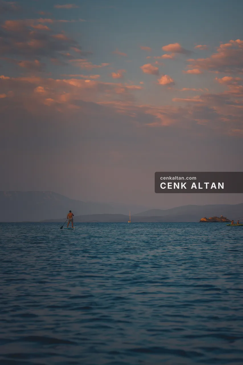 Pembe alacakaranlıkta denizde tek bir kişi ve uzakta dağlar