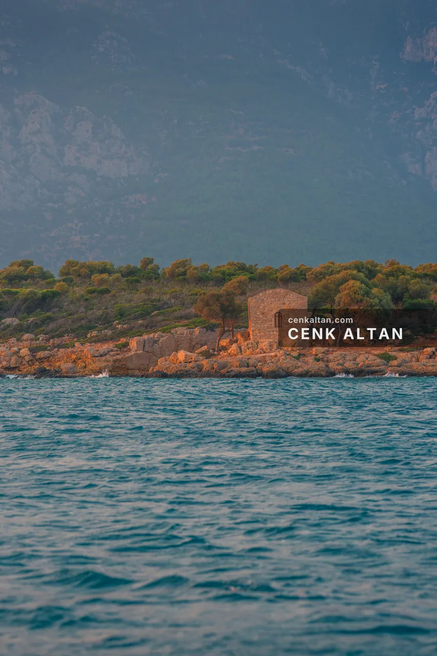 Küçük bir adada taş ev ve çevresinde ağaçlar, deniz